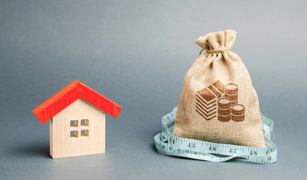 Bag with money and tape measure with a wooden house. The concept of a limited real estate budget. Low subsidies. Lack of investment in construction. Market crisis. Reduced demand for home buying
