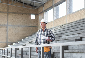 Portrait of senior construction worker with blueprint controlling building site.