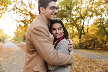 Image of young brunette couple smiling and hugging in autumn park