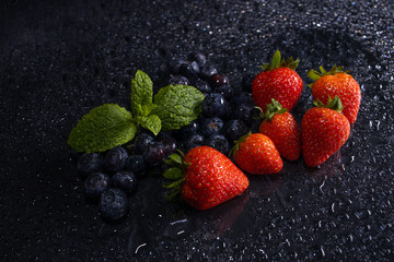 fresh red strawberries and blueberries macro on black table waterdrops