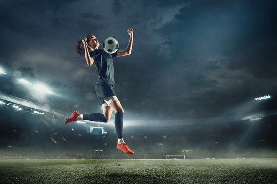 Young female soccer or football player with long hair in sportwear and boots kicking ball for the goal in jump at the stadium. Concept of healthy lifestyle, professional sport, hobby, motion, movement