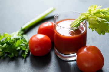 glass of tomato juice with celery, fresh tomatoes on black background