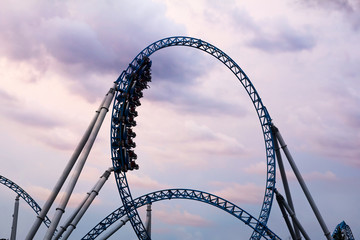 Silhouette of people having fun on a roller-coaster in an amusement park at sunset. Adrenalin...