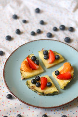 Plate with pineapple 'pizzas' - slices of pineapple with strawberries, tangerines and blueberries. Selective focus.