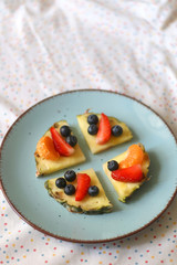Plate with pineapple 'pizzas' - slices of pineapple with strawberries, tangerines and blueberries. Selective focus.