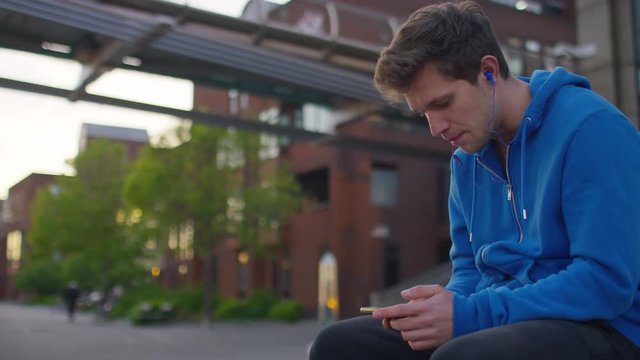 Young man listening to his music is beat boxing along to it as he sits out in the city