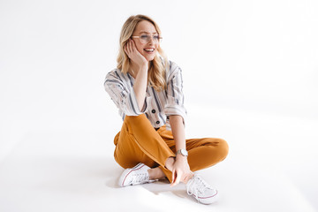Portrait of blond smiling woman wearing glasses propping her head and looking aside while sitting...