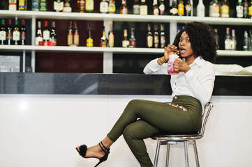 Сheerful business african american lady with afro hair, wear white blouse and green pants sitting...