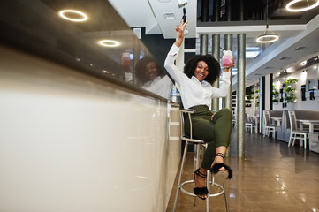Сheerful business african american lady with afro hair, wear white blouse and green pants sitting...