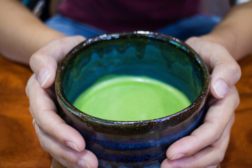 Fototapeta na wymiar Hand on bowl of hot matcha green tea drink