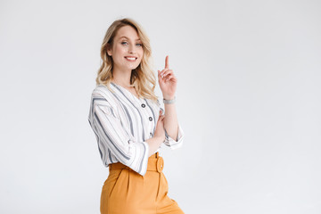 Half turn portrait of young woman wearing casual clothes smiling at camera and pointing finger upward