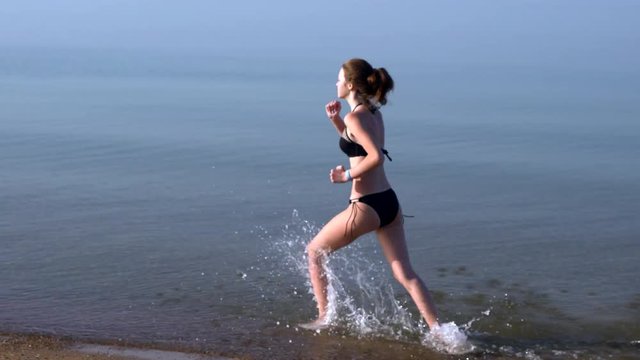 Slim young woman running through shallow sea