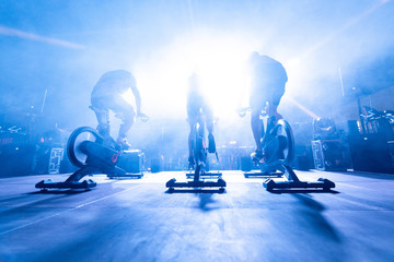 spinning instructors on stage,  before a group of people doing spinning on cycle bike