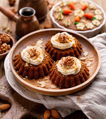 Carrot-nut muffins with mascarpone cream decorated with walnuts, pine nuts and cinnamon on a wooden plate. Delicious dessert