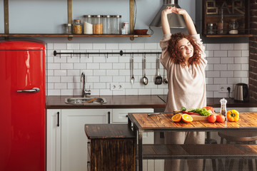 Image of attractive young woman smiling while cooking salad with fresh vegetables at home