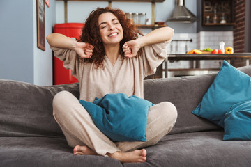 Photo of relaxed young woman smiling and sitting on sofa in apartment