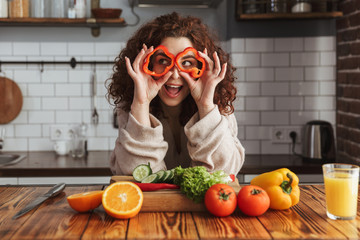 Photo of young caucasian woman smiling while cooking salad with fresh vegetables at home