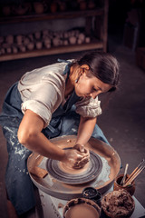 Charming artisan woman creates a new pottery from clay on a potter's wheel. Folk handicraft.