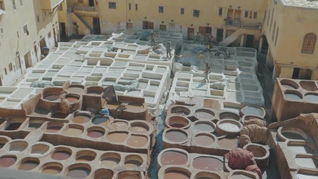 Overlooking the famous Tannery in Fez, Morocco with stone vessels filled with a colorful dyes as a historical tradition to dye materials panning through a metal fence with transitions at the end