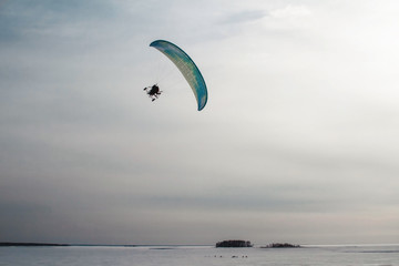 Fototapeta na wymiar Paraglider with motor flies over the sea, which is covered with ice and snow. Free flight in winter