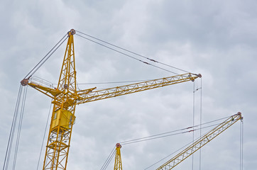 Two yellow construction crans on the cloudy sky background, the view from the bottom up.