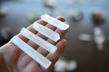 Woman's hand holding miniature selenite rods. Bright white healing selenite. Macro photo of healing crystals in hand, selenite chunks. Wiccan spell wands. 