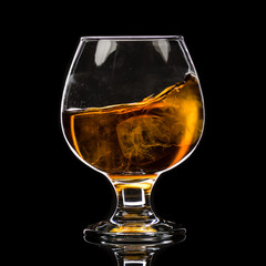 A round glass of whiskey brandy with ice, a wave and a small splash
