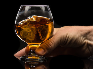A round glass of whiskey brandy with ice in the men's hand