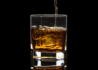 Hexagonal glass of whiskey brandy with ice and splashes from falling ice