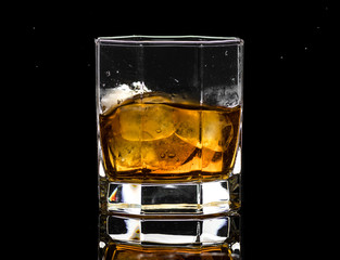 Hexagonal glass of whiskey brandy with ice and splashes from falling ice