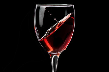 A glass of wine with red wine hovering at an angle and a fallen drop, the horizon is shifted