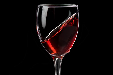 A glass of wine with red wine hovering at an angle and a fallen drop, the horizon is shifted