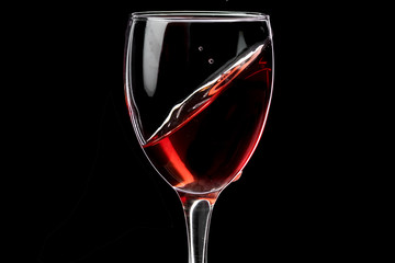 A glass of wine with red wine hovering at an angle and a fallen drop, the horizon is shifted