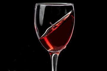 A glass of wine with red wine hovering at an angle and a fallen drop, the horizon is shifted