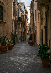 Fototapeta na wymiar Typical italian street with plants in pots without people in the Ortigia island in Siracusa, Sicily, south Italy