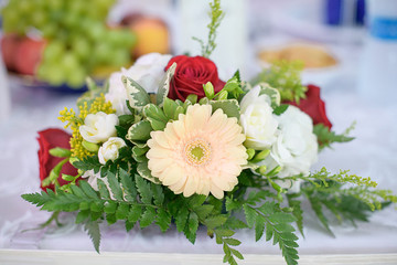 Romantic wedding decor for bride and groom or guests dinner tables at the reception venue or restaurant with beautiful floral centerpieces featuring red roses, pastel Gerbera daisies and greenery