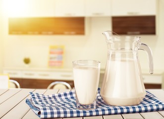 A glass of milk and a milk jug on plaid tablecloth