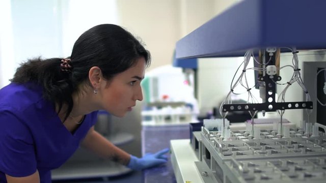 Portrait young lab woman in blue uniform and rubber gloves controlling drug manufacturing in the laboratory. Conducting research in the lab. Science, profession, healthcare. Slow motion