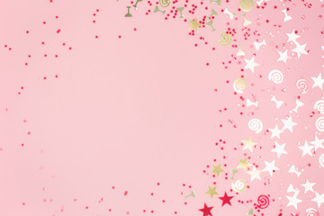 Golden stars flutes and swirls glitter and assorted sparkling confetti partially blurred on trendy pastel pink background. Festive holiday pastel backdrop with blank copy space.