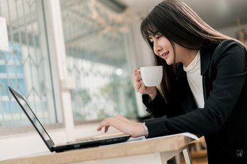 Business woman holding coffee mug in morning, She working on the laptop.