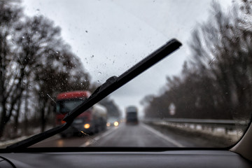 Photo through the windshield of the car in the raining evening, in the blur lights, track, trucks
