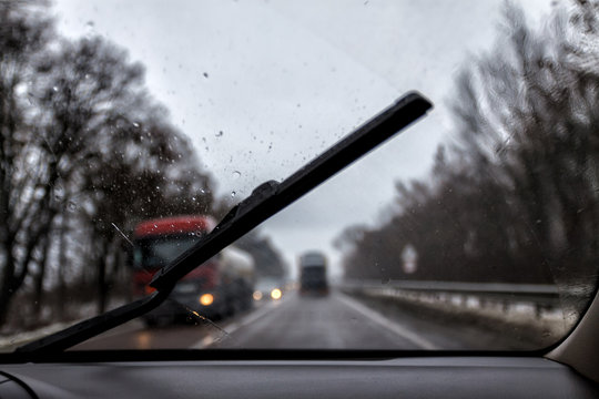 Photo through the windshield of the car in the raining evening, in the blur lights, track, trucks