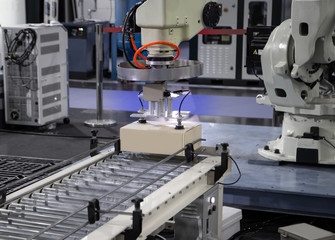 Industrial robot arm loading carton on conveyor in manufacturing warehouse.