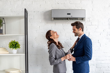 cheerful businesspeople laughing while standing under air conditioner in office