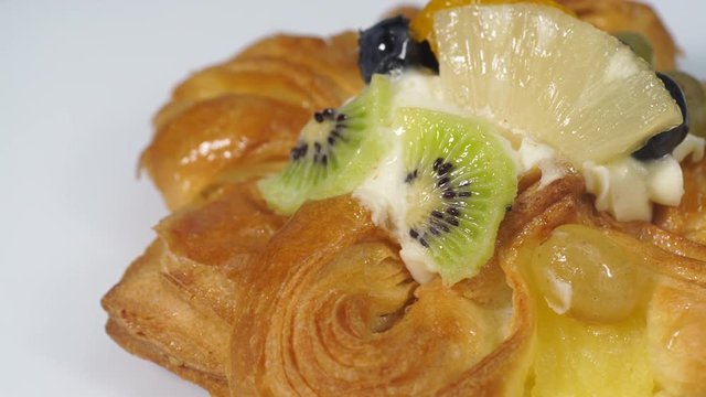 Close up puff pastry pie decorated with fresh blueberry and fruit slices - kiwi, grapes, ananas. Cake rotating