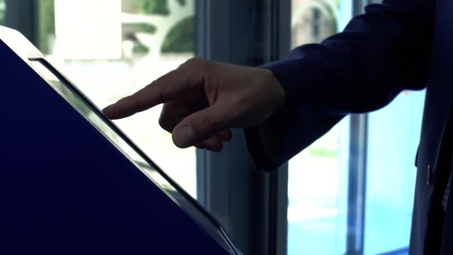 Close up male hand takes a ticket to the queue at the clinic. Hand of the man in the suit using terminal close up. The man touching the screan with his finger. Servise of the client