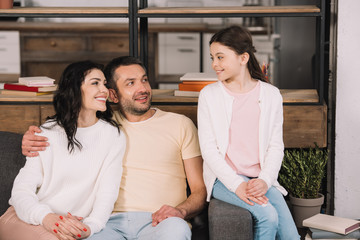 happy kid looking at cheerful parents sitting on sofa