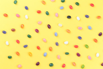 Colorful assorted jelly bean sweets on bright yellow background in flat lay with copy space. Party or celebration backdrop