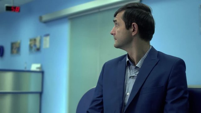 Mature man sit with ticket number in queue