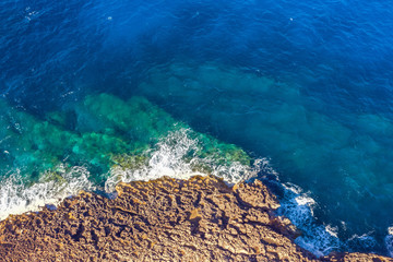 Sea coast on rocky beaches with turquoise water waves, aerial view.
